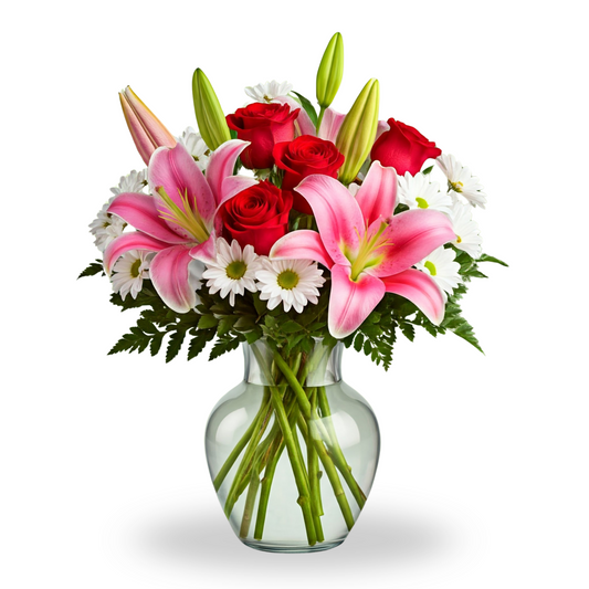 A romantic bouquet featuring pink lilies, red roses, and white daisies, arranged in a classic hourglass-shaped clear glass vase with soft greenery.